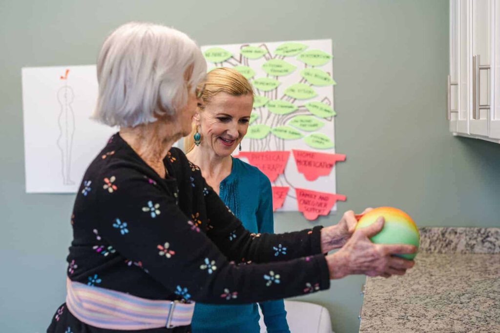 Senior woman holding weighted ball with physical therapist monitoring